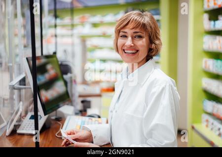 Buona donna farmacista in piedi in negozio medico Foto Stock