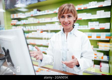 Donna sorridente farmacista gesturing al banco in negozio medico Foto Stock