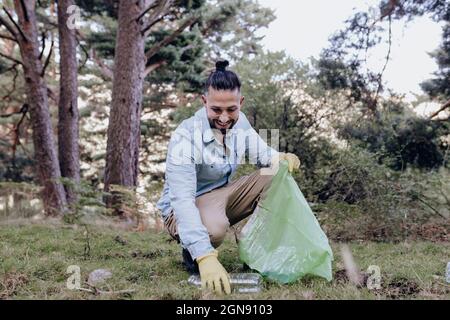 Maschio volontario raccogliere bottiglia di plastica mentre accovacciato nella foresta Foto Stock