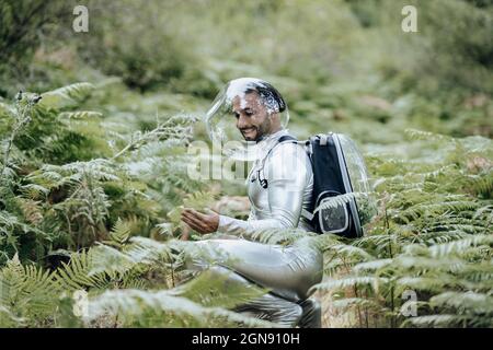 Un ambientalista maschile sorridente con tuta protettiva che esamina le piante nella foresta Foto Stock