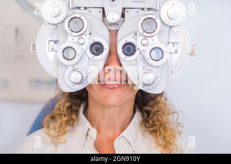 Sorridente paziente femmina che esamina la vista attraverso il foropter in clinica medica Foto Stock