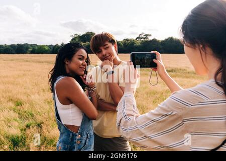 Donna fotografando amici con mano sul mento attraverso la macchina fotografica al parco Foto Stock