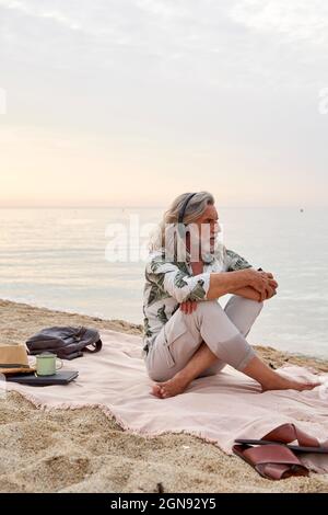 Uomo che abbraccia le ginocchia mentre ascolta la musica in spiaggia Foto Stock