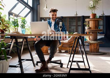 Uomo d'affari seduto con computer portatile podcasting in ufficio Foto Stock