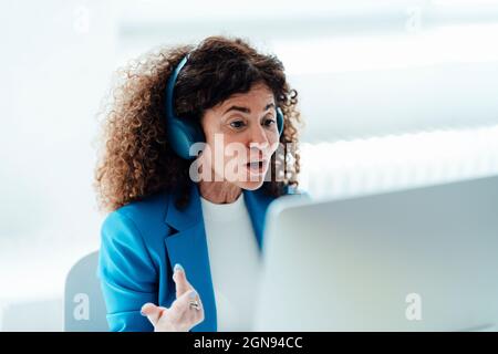Donna d'affari matura che indossa le cuffie mentre lavora alla scrivania in ufficio Foto Stock