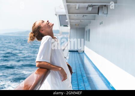 Donna sorridente con testa indietro appoggiata sulla ringhiera durante l'estate in traghetto Foto Stock