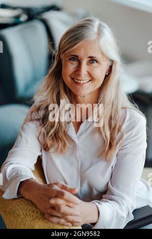 Donna matura sorridente con lunghi capelli grigi in caffetteria Foto Stock
