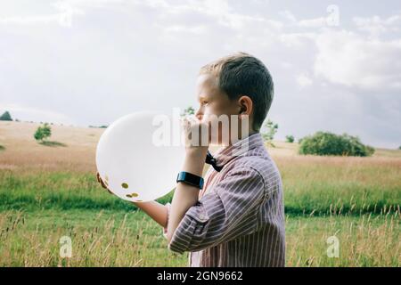 ragazzo vestito in modo intelligente che soffia un pallone in occasione di un matrimonio in estate Foto Stock