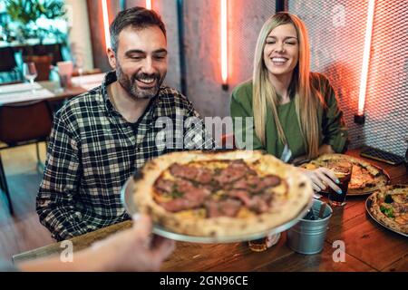 Donna che offre pizza ad amici maschi e femmine in ristorante Foto Stock