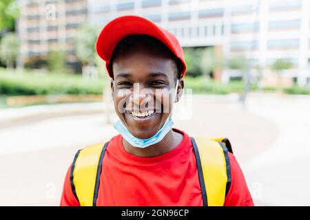 Uomo di consegna sorridente che indossa il cappello rosso durante il COVID-19 Foto Stock