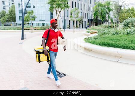 Persona giovane con zaino e pacchetto a piedi sul sentiero in città Foto Stock