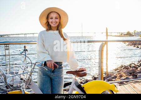Donna sorridente in piedi con la bicicletta sul lungomare Foto Stock
