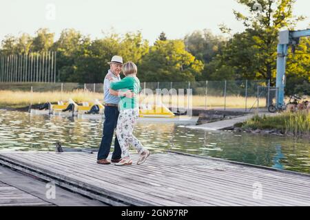 Felice coppia danzante senior sul molo vicino al lago Foto Stock