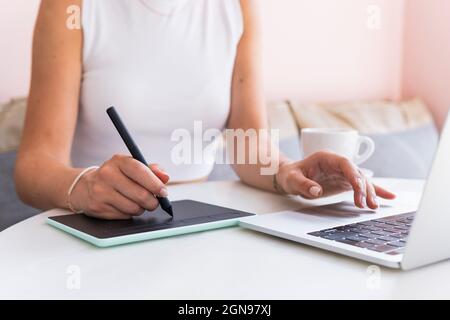 Professionista di design femminile che utilizza un notebook e un tablet grafico in un bar Foto Stock