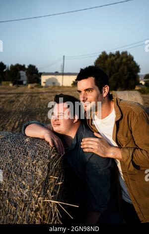 Amici maschi appoggiati su una balla di paglia durante il tramonto Foto Stock