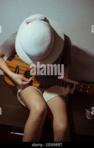 Una ragazza in un cappello di paglia e pantaloncini, giocando l'ukulele piegato sopra Foto Stock