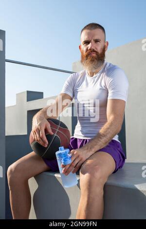 Un atleta fidato di sesso maschile in abbigliamento sportivo che tiene una bottiglia di acqua fredda e guarda la fotocamera Foto Stock