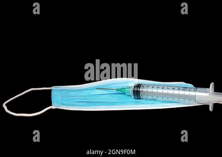 Siringa medica su carta blu usa e getta maschera isolato su nero Foto Stock