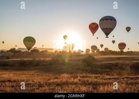 Un mazzo di palloncino colorato ad aria calda che vola la mattina presto contro l'alba in Cappadocia, Turchia contro la formazione di roccia tipica a causa dell'attività vulcanica i Foto Stock