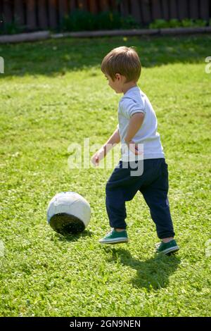 Ragazzo giovane che gioca a calcio da solo nel giardino di casa durante l'estate Foto Stock