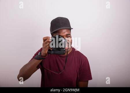 Il fotografo scatta una foto mentre guarda attraverso il mirino della fotocamera. Fotografo africano isolato su sfondo bianco. Foto Stock