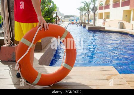 Primo piano di un anello salvagente con corda tenuta da un bagnino con piscina sullo sfondo. Bagnino durante il concetto di lavoro Foto Stock