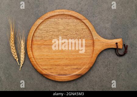 Piatto di pizza vuoto in legno con spighe di grano su sfondo di cemento scuro. Foto Stock
