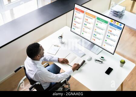 Afro American Man in Wheelchair con Kanban Software su computer Foto Stock