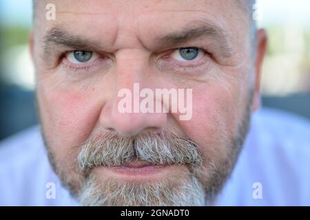 Uomo anziano con bearded che staring intently nell'obiettivo in una vista ravvicinata del suo volto con messa a fuoco ai suoi occhi grigio-blu Foto Stock