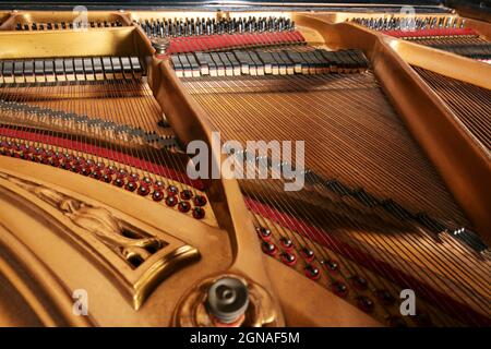 All'interno di un vecchio pianoforte con telaio in metallo dipinto d'oro, archi, martello, smorzatore e feltro rosso, che mostra la meccanica dell'istro musicale acustico Foto Stock
