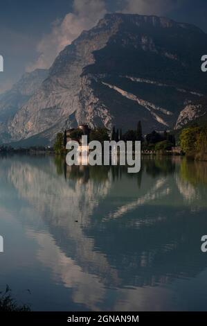 Le falesie dolomitiche sovrastano un castello medievale su un lago alpino, Castel Toblino sul Lago di Toblino in Trentino-Alto Adige. Il castello, visto qui la mattina presto di settembre, dalla riva settentrionale del lago, fu fondato negli anni '1100s e fu una volta residenza estiva per i potenti principi-vescovi di Trento. Foto Stock