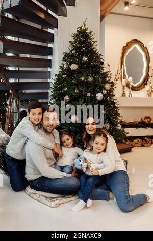 Ritratto di grande famiglia felice seduta vicino decorato albero di Natale, sorriso e coccole. Amare i genitori con i bambini gioiosi divertirsi in inverno Foto Stock