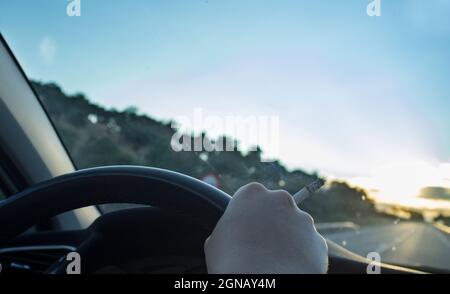 Donna che fuma durante la guida. Concetto di causa di incidenti stradali distratti. Vista interna dell'auto Foto Stock