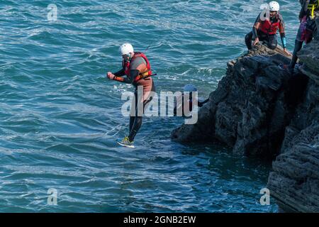 I vacanzieri saltano dalle rocce costellando con una guida su Towan Head a Newquay in Cornovaglia. Foto Stock