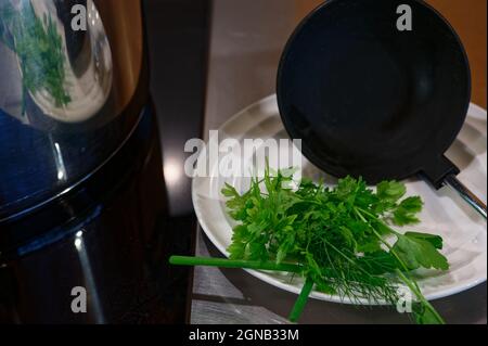 Le erbe verdi si siedono su un piatto con un mestolo della zuppa, stanno aspettando di essere aggiunte alla pentola della zuppa. Foto Stock