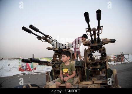 Teheran, Iran. 23 settembre 2021. I ragazzi posano con una pistola anti-aerea mentre visitano una mostra di guerra che è tenuta e organizzata dal corpo di Guardia rivoluzionaria Islamica (IRGC) in un parco nel sud di Teheran per celebrare l'anniversario della guerra Iran-Iraq (1980-88) il 23 settembre 2021. (Foto di Sobhan Farajvan/Pacific Press) Credit: Pacific Press Media Production Corp./Alamy Live News Foto Stock