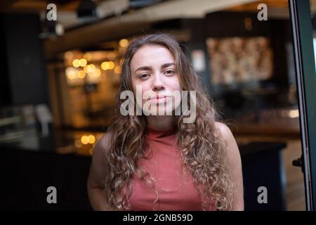 Giovane donna europea con capelli ricci scuri nel ritratto del ristorante Foto Stock
