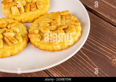 Gruppo di tre deliziosi biscotti interi con arachidi su piastra di ceramica bianca su legno marrone Foto Stock