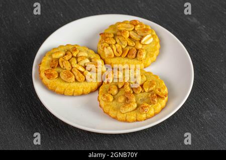 Gruppo di tre deliziosi biscotti interi con arachidi su piastra di ceramica bianca su pietra grigia Foto Stock