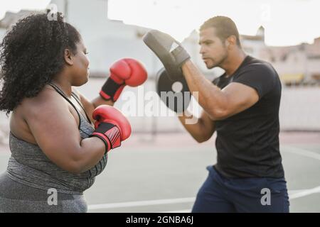 Donna curvy africana e personal trainer fare boxing sessione di allenamento all'aperto - fuoco sul braccio sinistro della ragazza Foto Stock