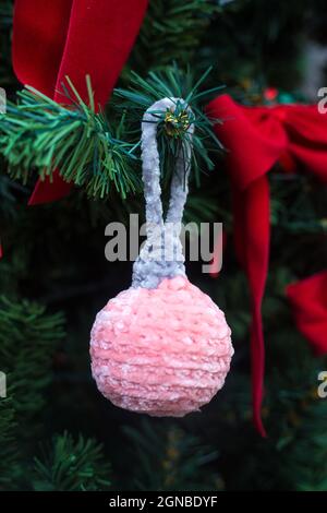 Amigurumi palla di Natale a maglia su albero di nuovo anno. Lussuosa decorazione artigianale di Natale. Giocattolo rosa con parte superiore grigia. Artigianato Foto Stock