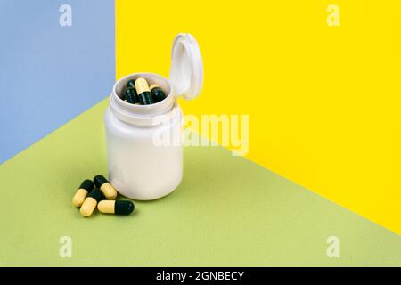 Pillole giallo-verdi in un vaso bianco su sfondi colorati. Integratore alimentare, multivitaminici, medicinali a base di erbe. Spazio di copia. Foto Stock