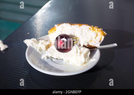 Dopo il concetto di festa di nuovo anno. Mattina del 1° gennaio. Pezzo di torta con panna montata su piatto bianco con cucchiaino da tè e pallina rossa di Natale su di esso. Inverno Foto Stock