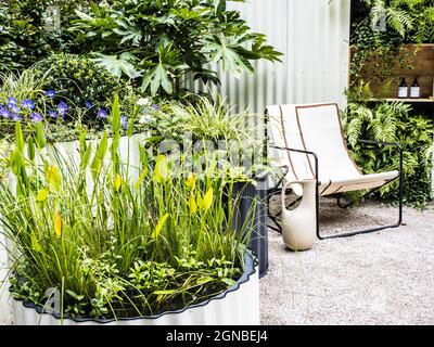 Un patio in ghiaia con sedia e contenitori riccamente piantati. Foto Stock