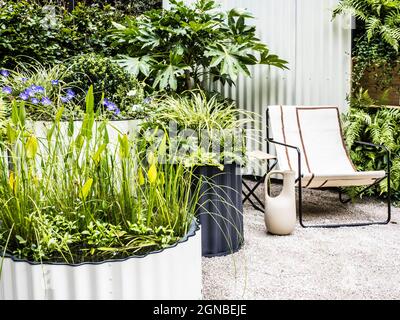 Un patio in ghiaia con sedia e contenitori riccamente piantati. Foto Stock