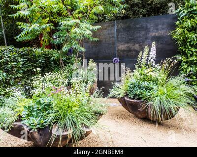 Un patio in ghiaia con sedia e contenitori riccamente piantati. Foto Stock