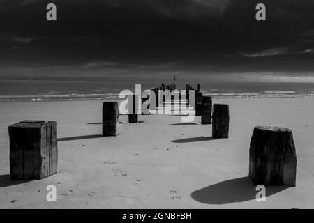 Immagine in bianco e nero di vecchi groynes, onde e sabbia sulla spiaggia di Lowestoft Suffolk UK. Nessuna gente Foto Stock