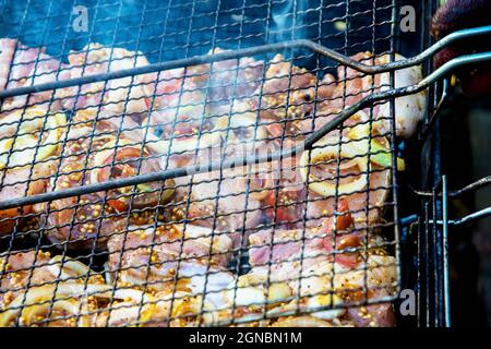 Pile marinate di maiale in salsa di soia e senape con anelli di cipolla e pomodori su una griglia, avvolta in fumo, orizzontale. Foto di alta qualità Foto Stock