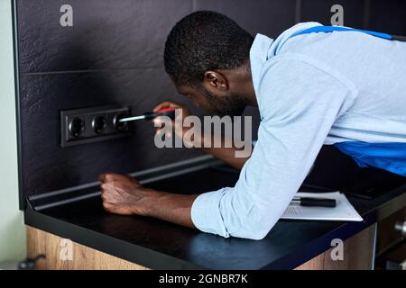 Elettricista sicuro, ripara, installa presa in cucina. Man master in bussole di torsione totale con cacciavite funzionante, riparazione. Maschio che lavora su t Foto Stock
