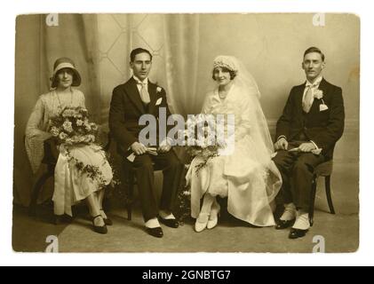 Splendido classico originale degli anni '20, era flapper, foto di gruppo di nozze ritratto, bella sposa indossando un velo lungo, splendida testata. seduto accanto allo sposo e al migliore uomo che indossa abiti coordinati con collari e spat per camicie alate. La bridesmaid o la cameriera d'onore indossa un cappellino alla moda, intorno al 1924, nel Regno Unito Foto Stock